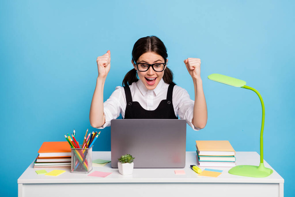 Photo of ecstatic girl sit table study remote use laptop celebrate a-level exam achievement raise fists scream wear style stylish trendy white blouse overall isolated blue color background - Photo, image