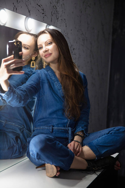 Charmante vrouw gekleed in denim overalls nemen van een selfie - Foto, afbeelding