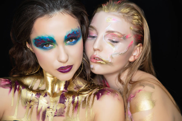 Two cute young women with creative make-up on the face posing in the studio. - Photo, Image
