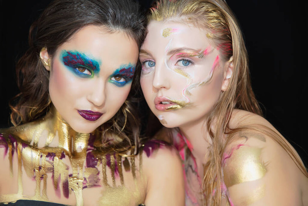 Twee mooie jonge vrouwen met creatieve make-up op het gezicht poseren in de studio. - Foto, afbeelding