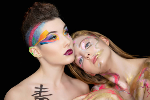Twee aantrekkelijke jonge vrouwen met creatieve make-up op het gezicht poseren in de studio. - Foto, afbeelding