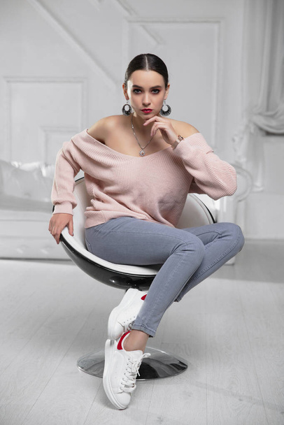 Charming brunette dressed in pink pullover and jeans sitting on an armchair - Foto, immagini