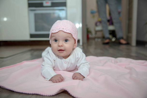 Beautiful little baby dressed in white sliders and a hat lies on a pink plaid - Foto, afbeelding
