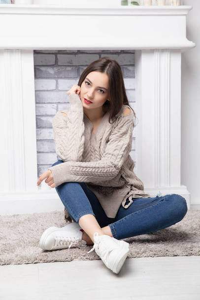 Beautiful young brunette dressed in pants and a sweater posing near the fireplace - Fotoğraf, Görsel