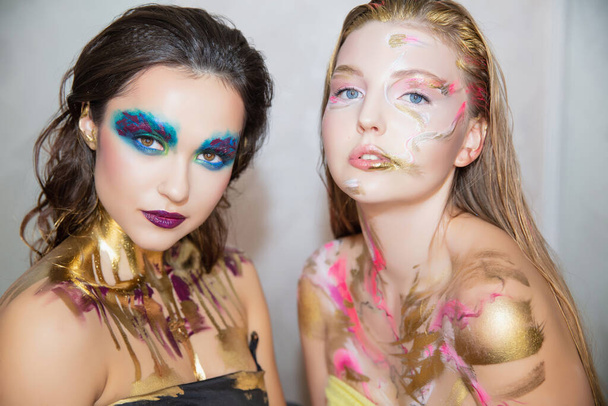 Dwie piękne, młode kobiety z kreatywnym makijażem na twarzy, pozujące w studio. - Zdjęcie, obraz