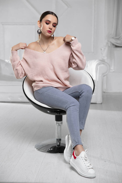 Ελκυστική μελαχρινή ντυμένη με ροζ πουλόβερ και τζιν σε πολυθρόνα - Φωτογραφία, εικόνα