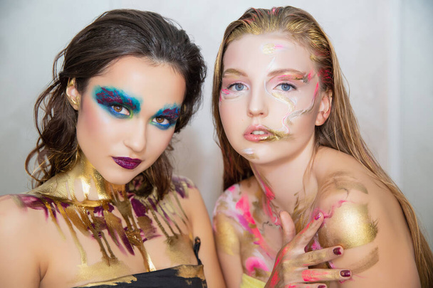 Zwei charmante junge Frauen mit kreativem Make-up im Gesicht posieren im Studio. - Foto, Bild
