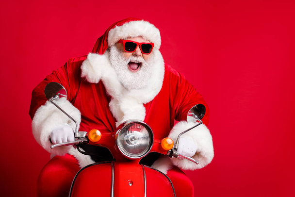 Photo of retired grandfather white beard ride retro scooter open mouth mad careless overtake slow cars fast have fun wear x-mas costume coat sunglass cap isolated red color background - Foto, Imagen