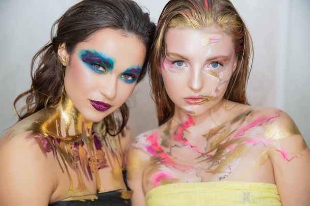 Zwei süße junge Frauen mit kreativem Make-up im Gesicht posieren im Studio. - Foto, Bild