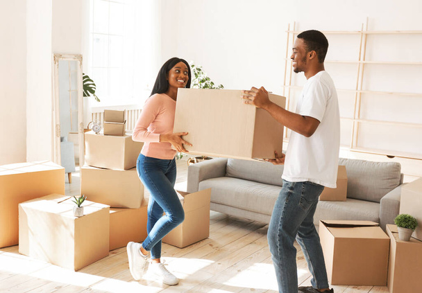 Повна довжина молодого чорного чоловіка зі своєю дівчиною, що носить картонну коробку в своєму новому будинку в рухомий день
 - Фото, зображення
