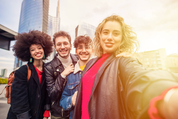 Grupo de amigos multiétnicos ao ar livre se divertindo e tirando selfie usando smartphone ao ar livre no cty com arranha-céus  - Foto, Imagem