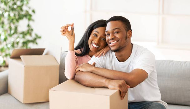 Heureux couple noir avec clé de maison et boîtes en carton regardant la caméra et souriant dans leur propriété, panorama - Photo, image
