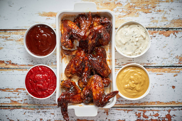 Chicken wings in thick barbecue sauce with various side dips. Served on white cast iron dish - Photo, Image