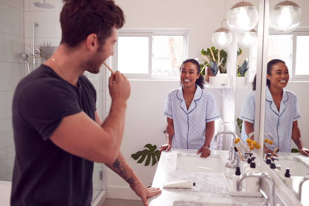 Pareja usando pijamas de pie en el baño en el fregadero cepillándose los dientes por la mañana - Foto, imagen