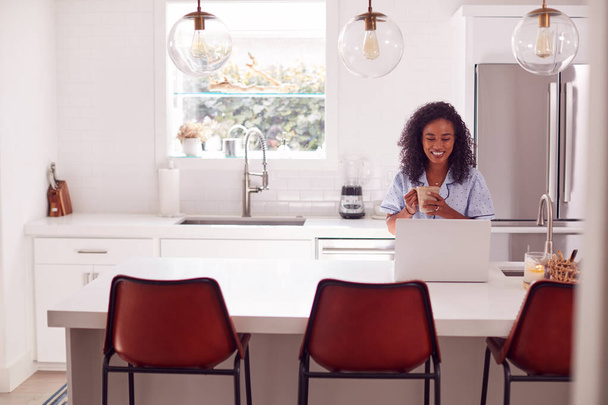 Woman Wearing Pyjamas Sitting In Kitchen Working From Home On Laptop - Photo, image