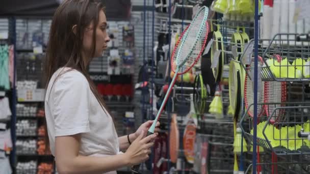 若い女性はスポーツショップでバドミントンラケットを購入しています - 映像、動画
