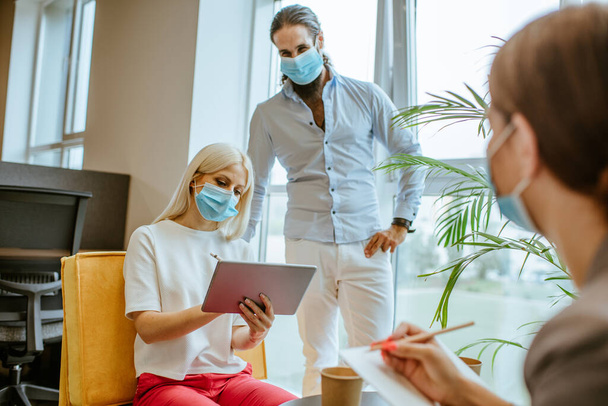 Jonge zakenmensen in beschermende medische maskers bespreken iets op kantoor tijdens de uitbraak van de wereldwijde pandemie COVID-19. Kantoorleven in een nieuw normaal. - Foto, afbeelding