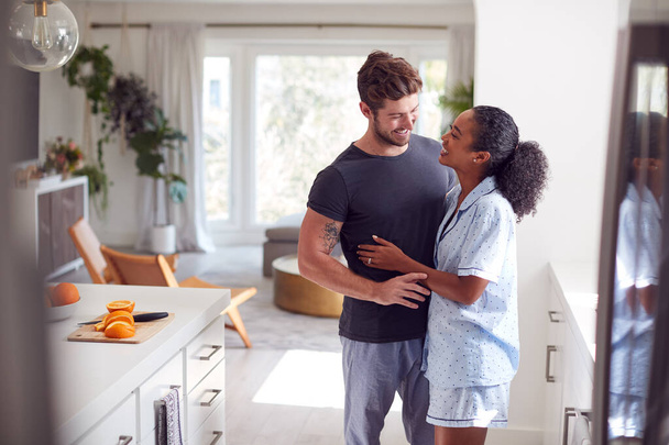 Loving Couple Wearing Pyjamas Hugging In Kitchen At Home Together - Photo, image