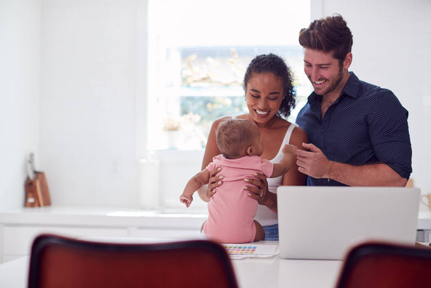 Family With Baby Daughter In Kitchen Using Laptop On Counter - Photo, Image