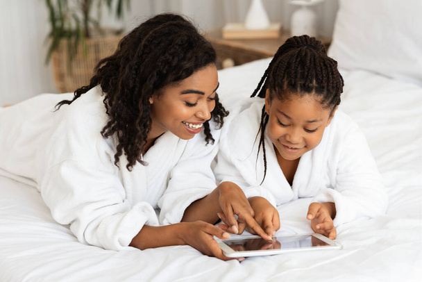 Happy African Mother And Little Daughter In Bathrobes Relaxing With Digital Tablet - Photo, Image
