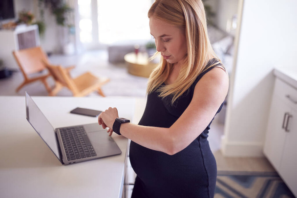 Pregnant Woman Checking Health Activity App On Smart Watch At Home On Laptop - Foto, afbeelding