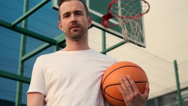Muž držící basketbal, stojící na venkovním hřišti - Záběry, video