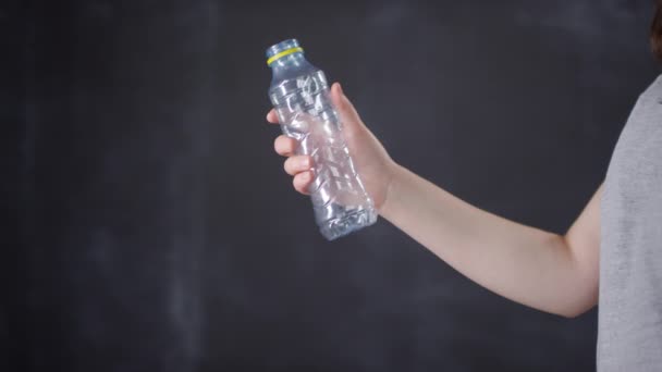 Midsection footage of female hand holding empty plastic bottle crushing it and throwing on ground on dark background - Footage, Video