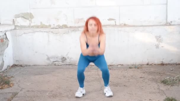 young red-haired girl athlete doing a warm-up, in a turquoise sports uniform leggings, against the background of a vintage street texture. active lifestyle. - Footage, Video