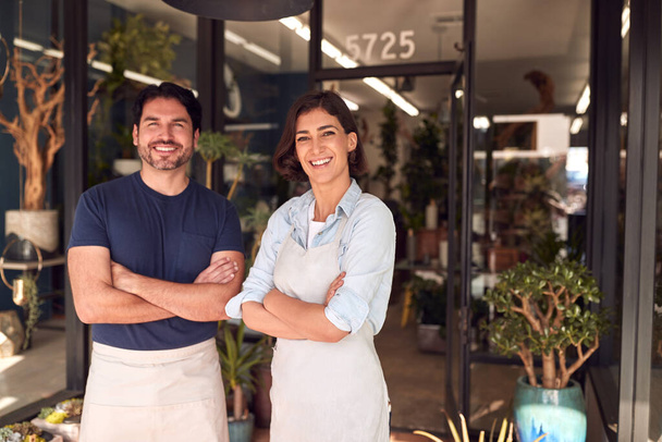 Portrait Of Smiling Male And Female Owners Of Florists Standing In Doorway Surrounded By Plants - Фото, изображение