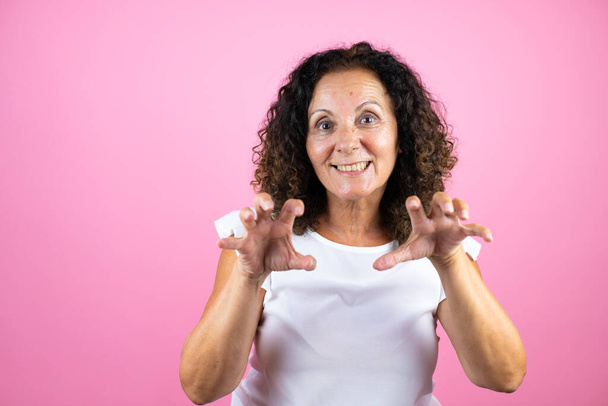 Mulher de meia idade vestindo camisa branca casual em pé sobre fundo rosa isolado sorrindo engraçado fazendo gesto garra como gato, expressão agressiva e sexy - Foto, Imagem