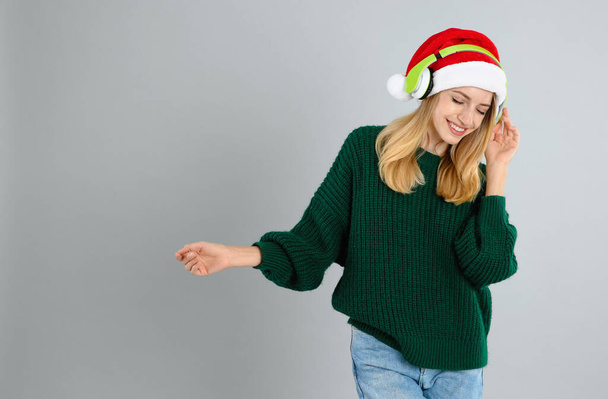 Happy woman with headphones on grey background, space for text. Christmas music - Фото, изображение