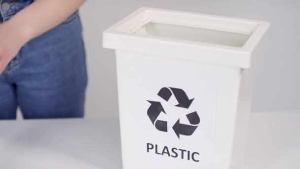 Plastiği seçici odak noktasında sıralamak için geri dönüşüm konteynırı ve tanınmayan eller beyaz arkaplana plastik şişeler koyuyor - Video, Çekim