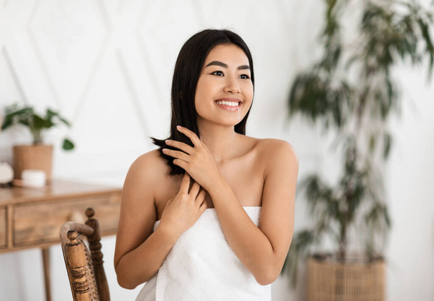 Houkutteleva hymyilevä aasialainen nainen soveltamalla hiustenhoito kotona - Valokuva, kuva