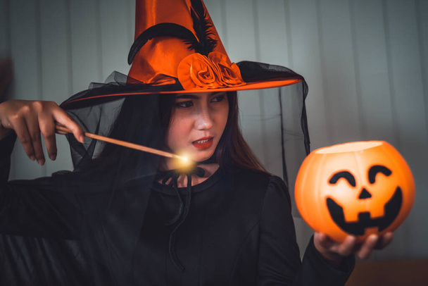 Aantrekkelijke mooie Aziatische vrouw verkleed als een heks met behulp van magische toverstaf casting spreuk naar jack pompoen hoofd, Halloween vakantie.  - Foto, afbeelding