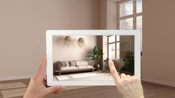 Augmented reality concept. Handtablet met AR-toepassing voor het simuleren van meubels en designproducten in leeg interieur met parket, moderne woonkamer met bank - Foto, afbeelding