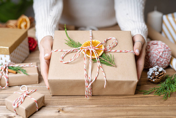 Női kezek csomagolása karácsonyi ajándék, közelről. Felkészületlen ajándékok fa háttér díszítő elemek és elemek, felülnézet. Karácsony vagy újév DIY csomagolási koncepció. Lépésről lépésre - Fotó, kép