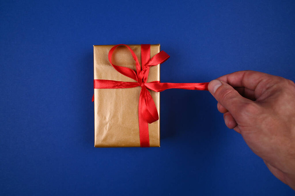 Hand untie gift wrapping on blue background. High quality photo - Fotografie, Obrázek