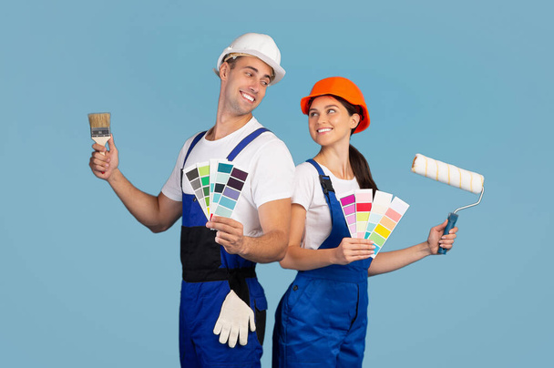 Vrolijk paar in harde hoeden poseren met verf borstels en kleurstalen - Foto, afbeelding
