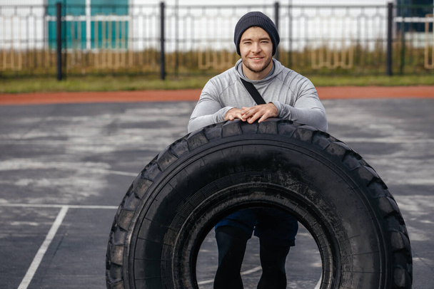 Třicetiletý silný sportovec odpočívající na pneumatice po tréninku na čerstvém vzduchu. Sportovní životní styl. - Fotografie, Obrázek