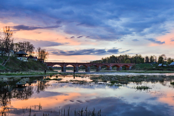 Landscape view of old brick bridge over river Venta in a late sunset evening. Photo taken in Spring, Latvia, Kuldiga. - Photo, Image