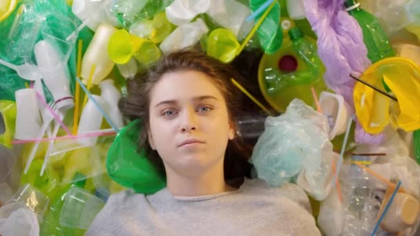 Top-view közelkép fiatal kaukázusi nő feküdt halom műanyag tárgyak nézi kamera szomorúan - Felvétel, videó