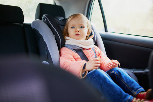 Adorable toddler girl in modern car seat eating cookie. Little kid traveling by car. Child safety on the road. Trip with a baby - Photo, Image