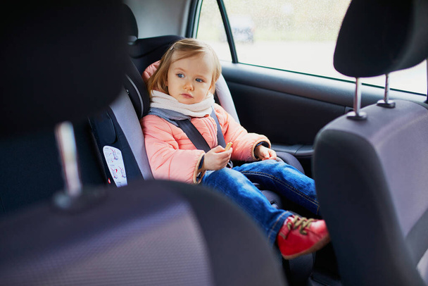 Adorable toddler girl in modern car seat eating cookie. Little kid traveling by car. Child safety on the road. Trip with a baby - Foto, immagini