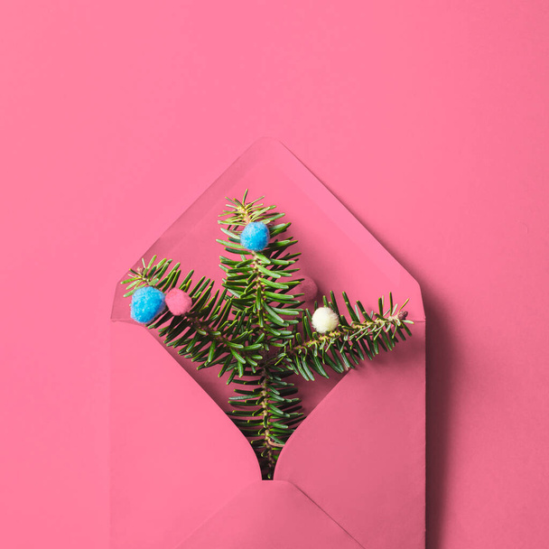 Розовый конверт с ветвями елки и безделушками на розовом фоне - Фото, изображение