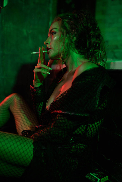Seksowna kobieta siedząca na podłodze w łazience, paląca i pijąca wino. Czerwone i zielone światło. Zdjęcia filmowe - Zdjęcie, obraz