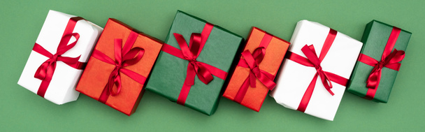website header van veelkleurige geschenkdozen met rode linten en strikken op groene achtergrond, bovenaanzicht - Foto, afbeelding