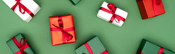 panoramic shot of colorful gift boxes with red ribbons and bows on green background, top view - Foto, Imagem