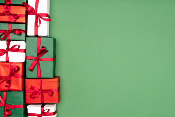 bovenaanzicht van veelkleurige geschenkdozen met rode linten op groene achtergrond met kopieerruimte - Foto, afbeelding