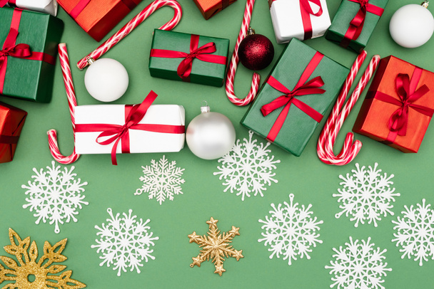 вид зверху різнокольорові подарункові коробки, цукерки, різдвяні кульки та декоративні сніжинки на зеленому фоні
 - Фото, зображення