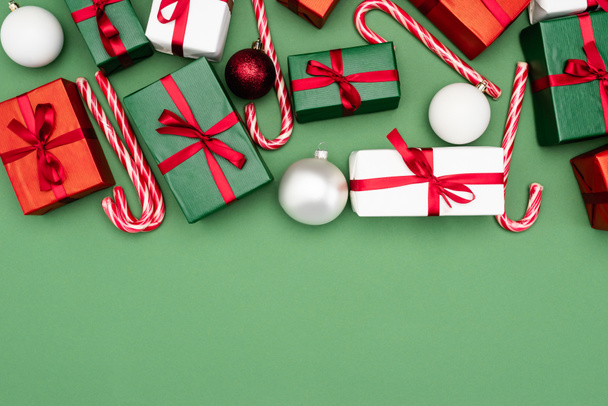top view of colorful gift boxes, candy canes and christmas balls on green background with copy space - Photo, Image
